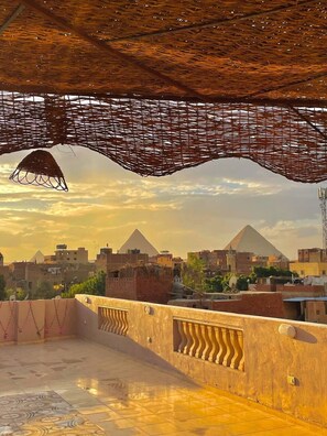 A rooftop terrace with a view of pyramids and a cityscape. - Four pyramids Guest house (Giza)