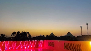 Una vista al atardecer con un edificio en forma de pirámide y una estructura iluminada en rojo en primer plano.