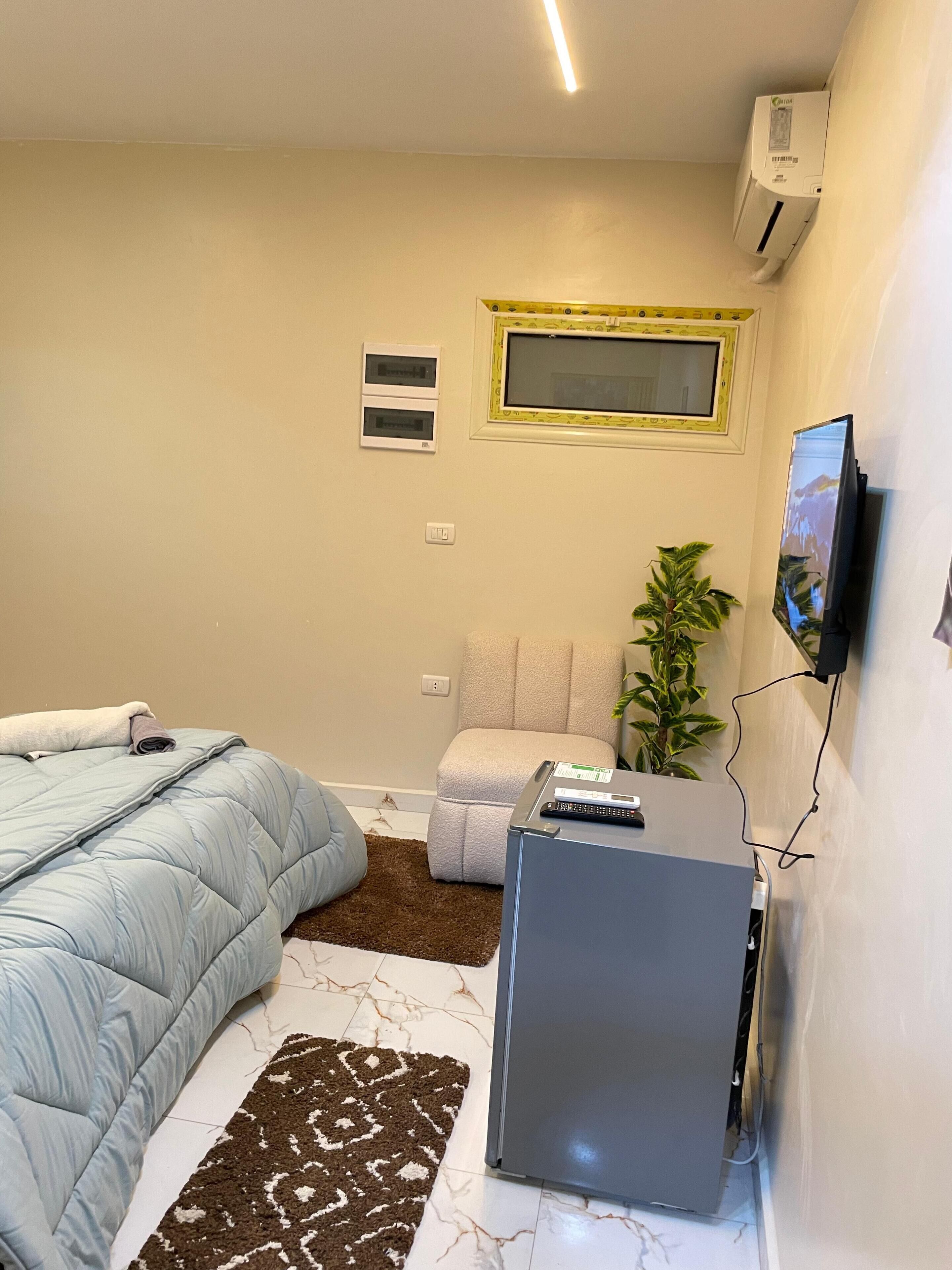 Un dormitorio con una cama, un escritorio pequeño, una silla, una planta y un televisor montado en la pared.