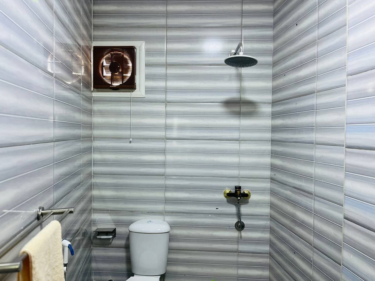 Un baño con ducha, inodoro y ventilador.