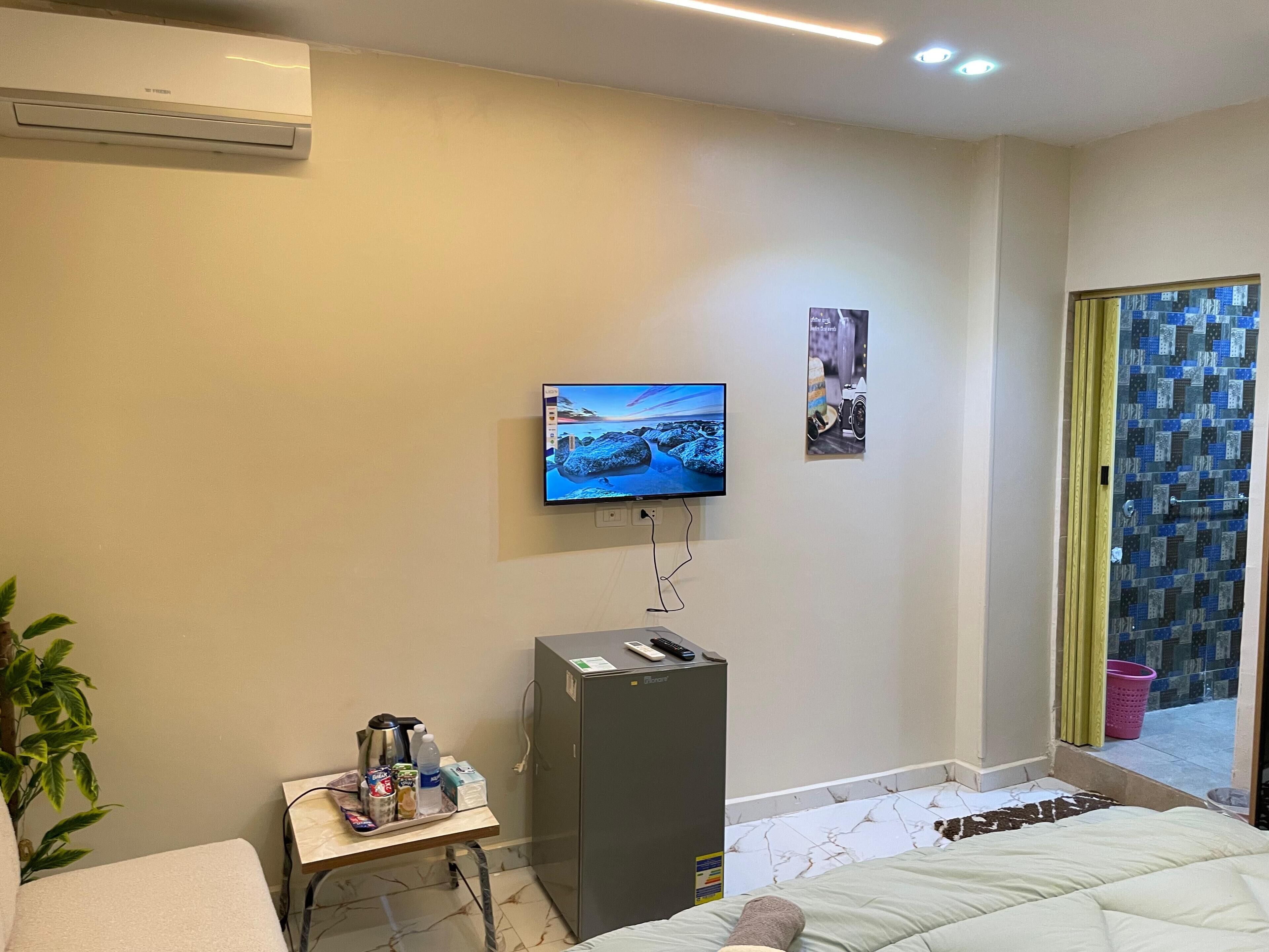 A hotel room with a bed, a desk with a coffee maker, a TV, and a refrigerator.