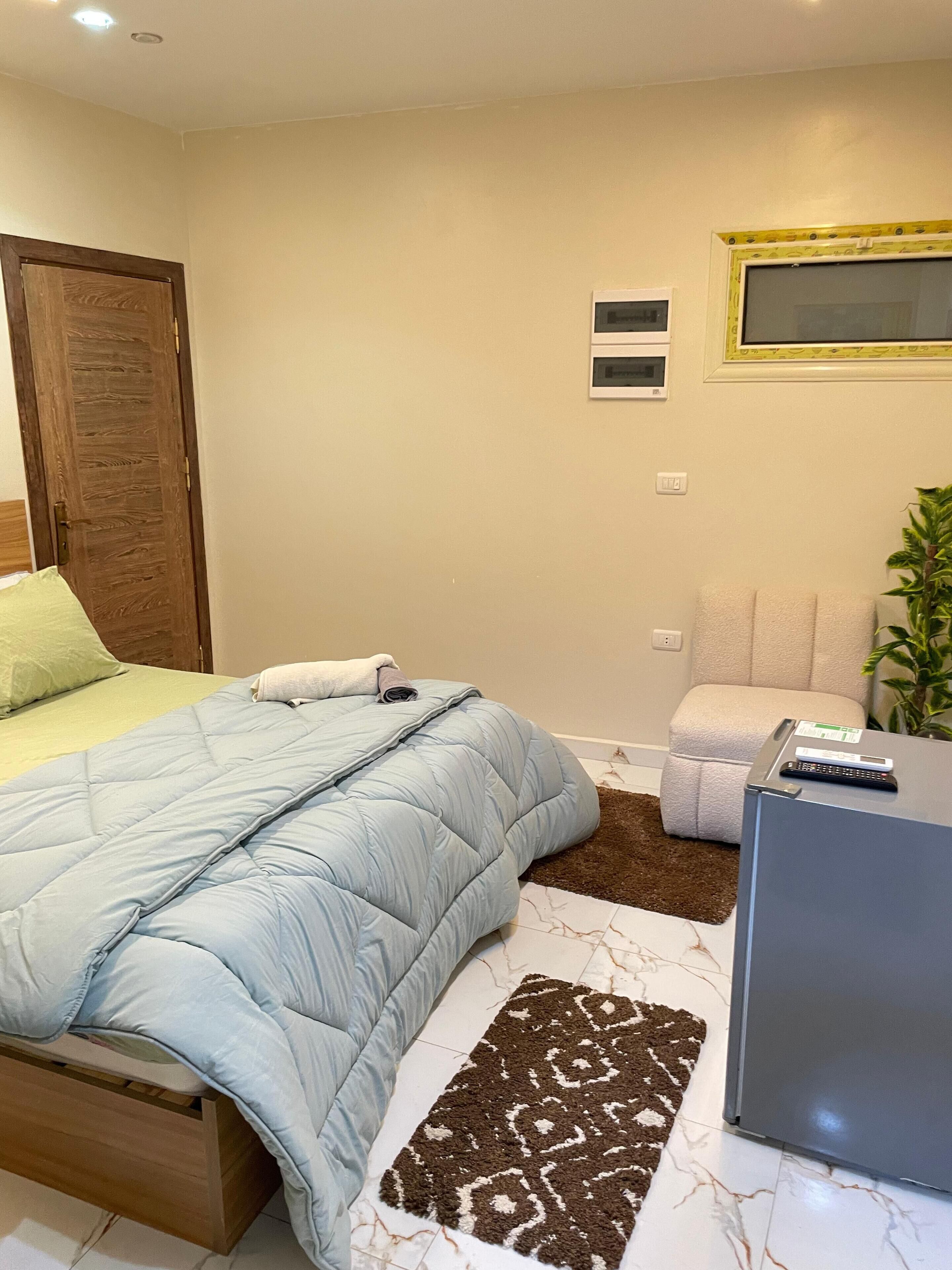 Ein Schlafzimmer mit einem Bett, einem kleinen Schreibtisch, einem Stuhl, einer Pflanze und einer Wandklimaanlage.