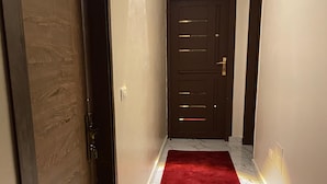 Un pasillo con puerta de madera, alfombra roja y suelo de mármol que conduce a una puerta de madera oscura.