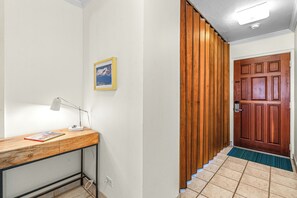 A hallway with a wooden desk, a framed picture on the wall, and a wooden door at the end. - Waiohuli Beach Hale A-103 Ocean Front Complex, Ocean View, Steps to the Beach (Kihei)