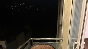 Ein Balkon mit einem Korbstuhl und einem kleinen, runden Tisch, beide mit gelben Kissen.