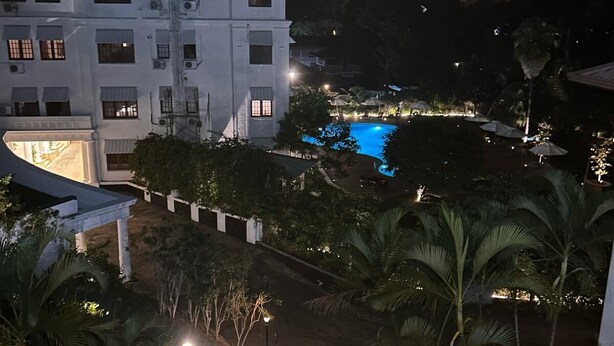 Ein Hotel mit einem Swimmingpool, umgeben von Palmen und einem weißen Gebäude mit vielen Fenstern.