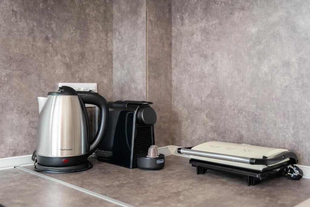 A kitchen with a stainless steel kettle, a coffee maker, and a portable electric kettle on a countertop.