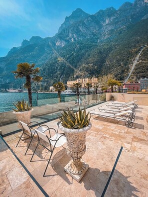 A terrace with outdoor seating, a palm tree, and a mountain backdrop. - Bellavista Lakefront Apartments  (Riva del Garda)