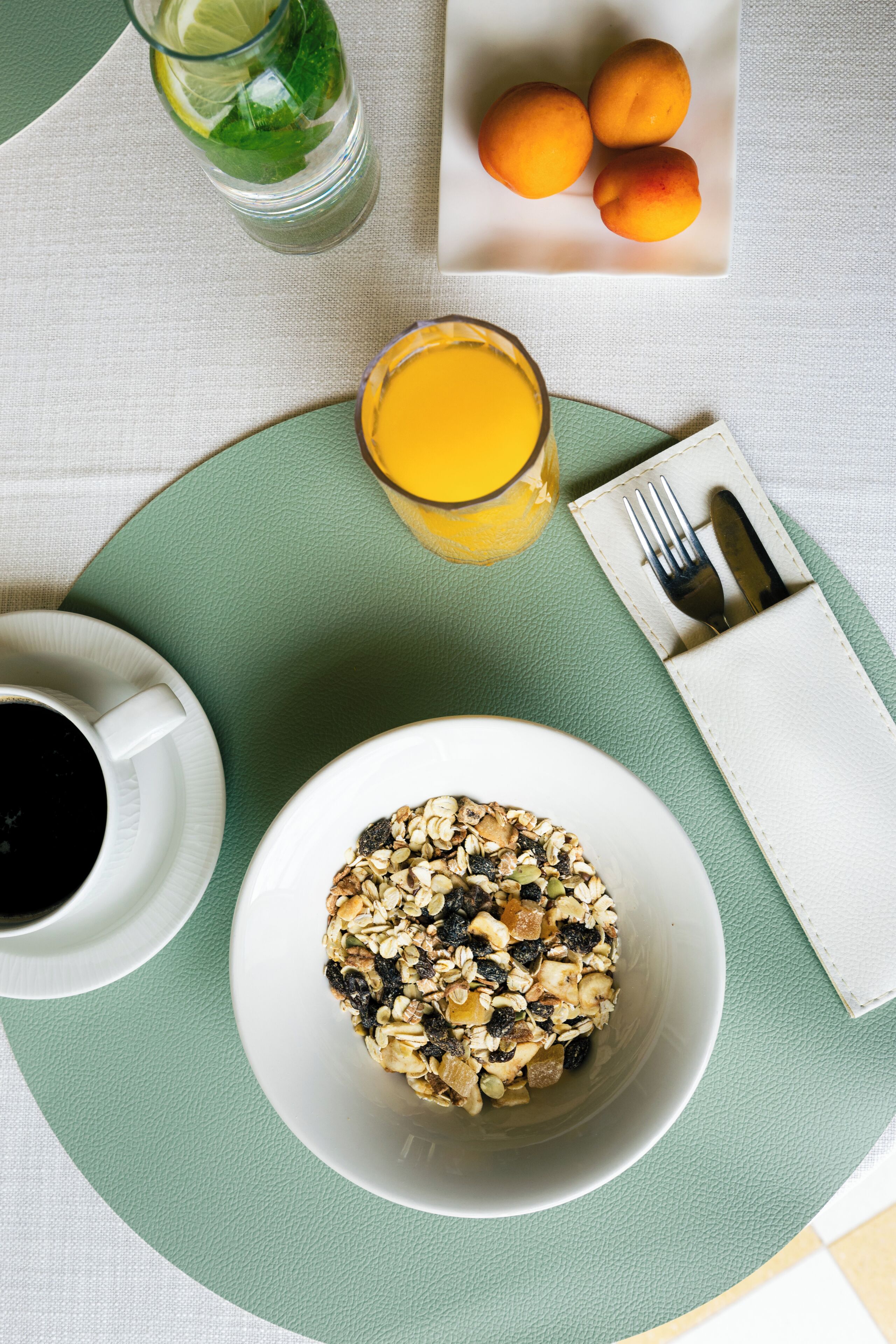 Un desayuno con un tazón de avena, un vaso de jugo de naranja y un plato de albaricoques sobre una mesa.