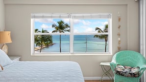 Une chambre avec une grande fenêtre donnant sur une plage, un lit, une chaise et une petite table.