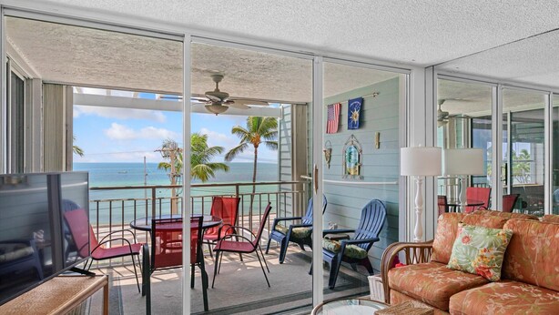 Un balcon avec vue sur l’océan, aménagé avec des chaises et une table, ainsi qu’un canapé avec des coussins.
