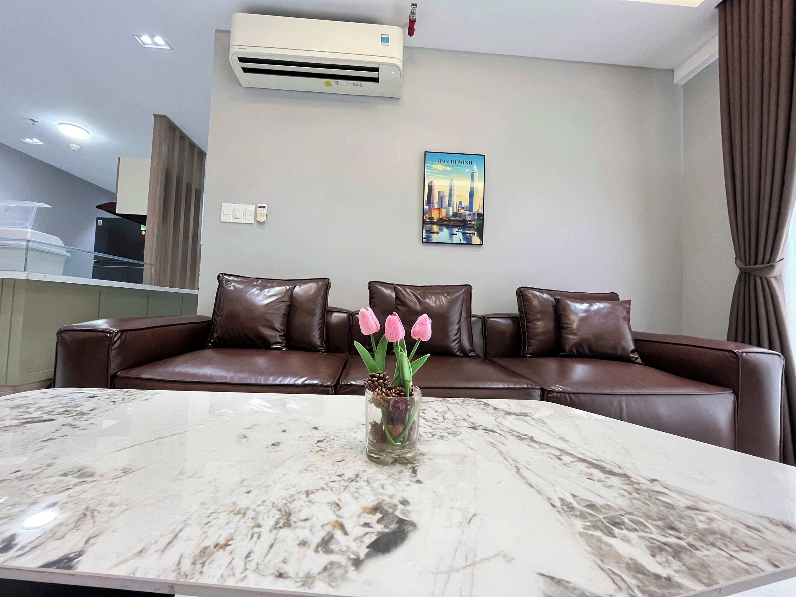 A modern living room with a brown leather sofa, a marble coffee table, and a wall-mounted air conditioner.