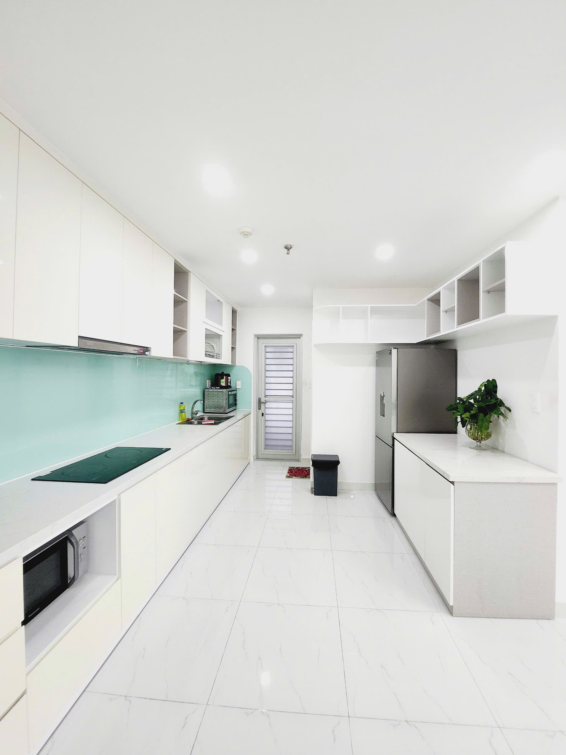 A modern kitchen with white cabinetry, a green backsplash, and a stainless steel refrigerator.