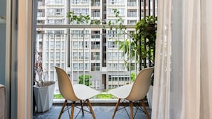 Een balkon met twee moderne stoelen, een plant in pot en uitzicht op een hoog gebouw.