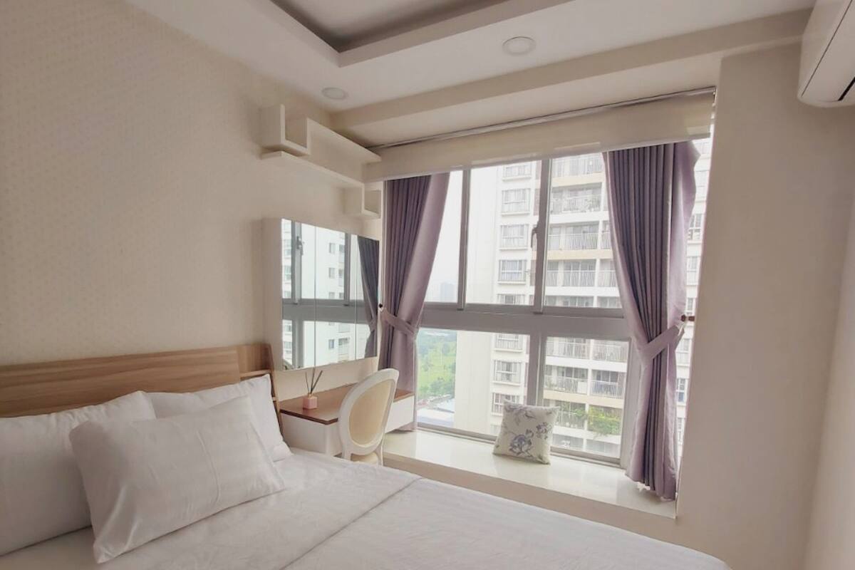 Une chambre à coucher avec un grand lit, un bureau et une chaise près d’une fenêtre avec des rideaux.