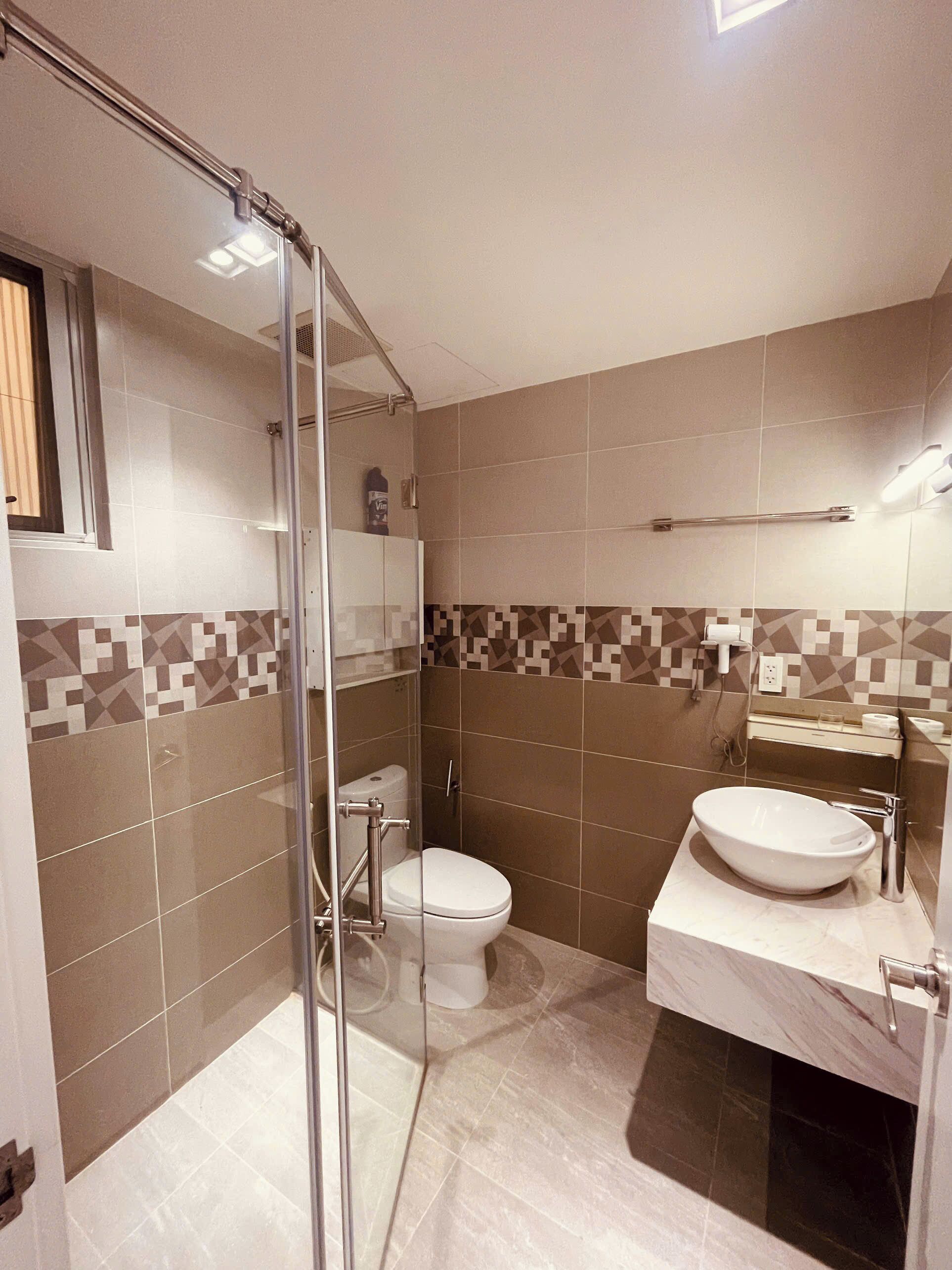 A bathroom with a glass shower enclosure, a toilet, and a sink with a marble countertop.