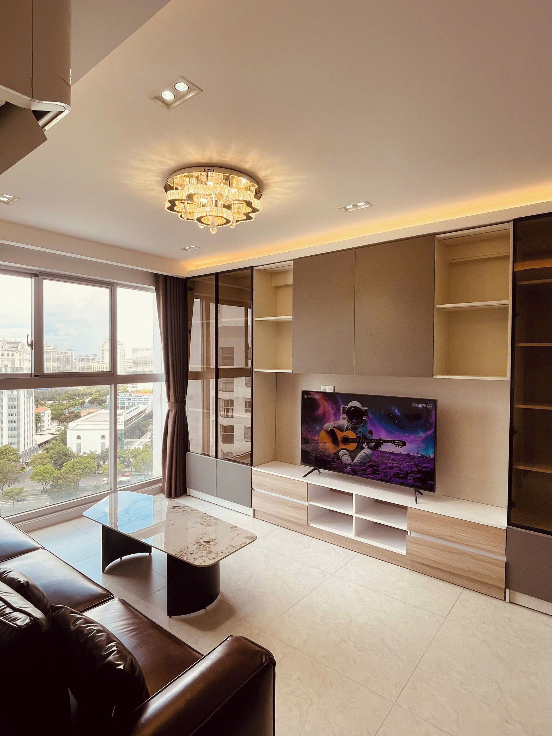 A modern living room with a large TV, a chandelier, and a city view.