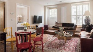 A living room with a TV, a sofa, a coffee table, and a dining area with chairs. - Upper Deck, The Upper Deck - Unique Harbourside 2Bed apartment with FREE Parking (Mevagissey)