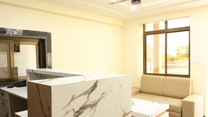 Una habitación de hotel moderna con una recepción de mármol, un sofá color beige y un ventanal con vistas al exterior.