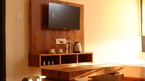 Una habitación moderna con televisión de pantalla plana montada en una pared de madera, una mesa de madera con tetera y tazas, y una cama con ropa blanca.