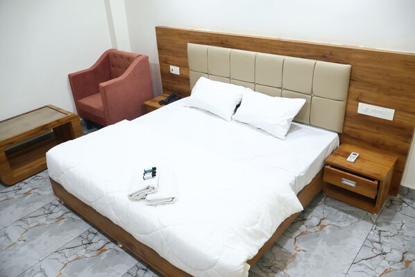 A hotel room with a large bed, a wooden headboard, a wooden nightstand with a phone, a pink chair, and a small wooden table.