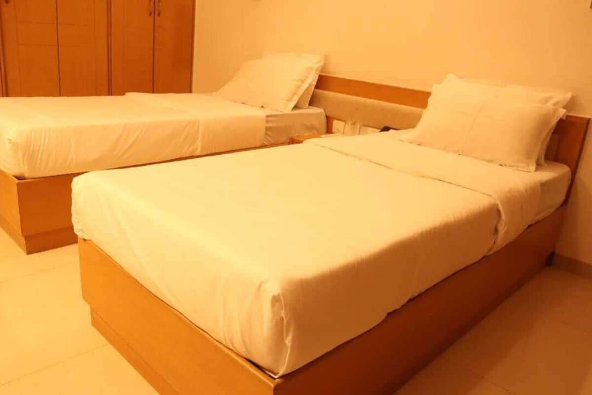 A room with two single beds, wooden headboards, and a tiled floor.