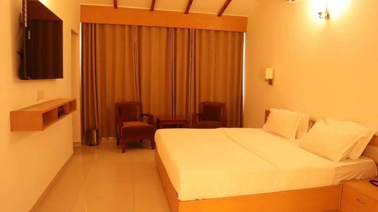 A hotel room with a large bed, a TV mounted on the wall, a desk with a chair, and a curtain separating the room from the hallway.