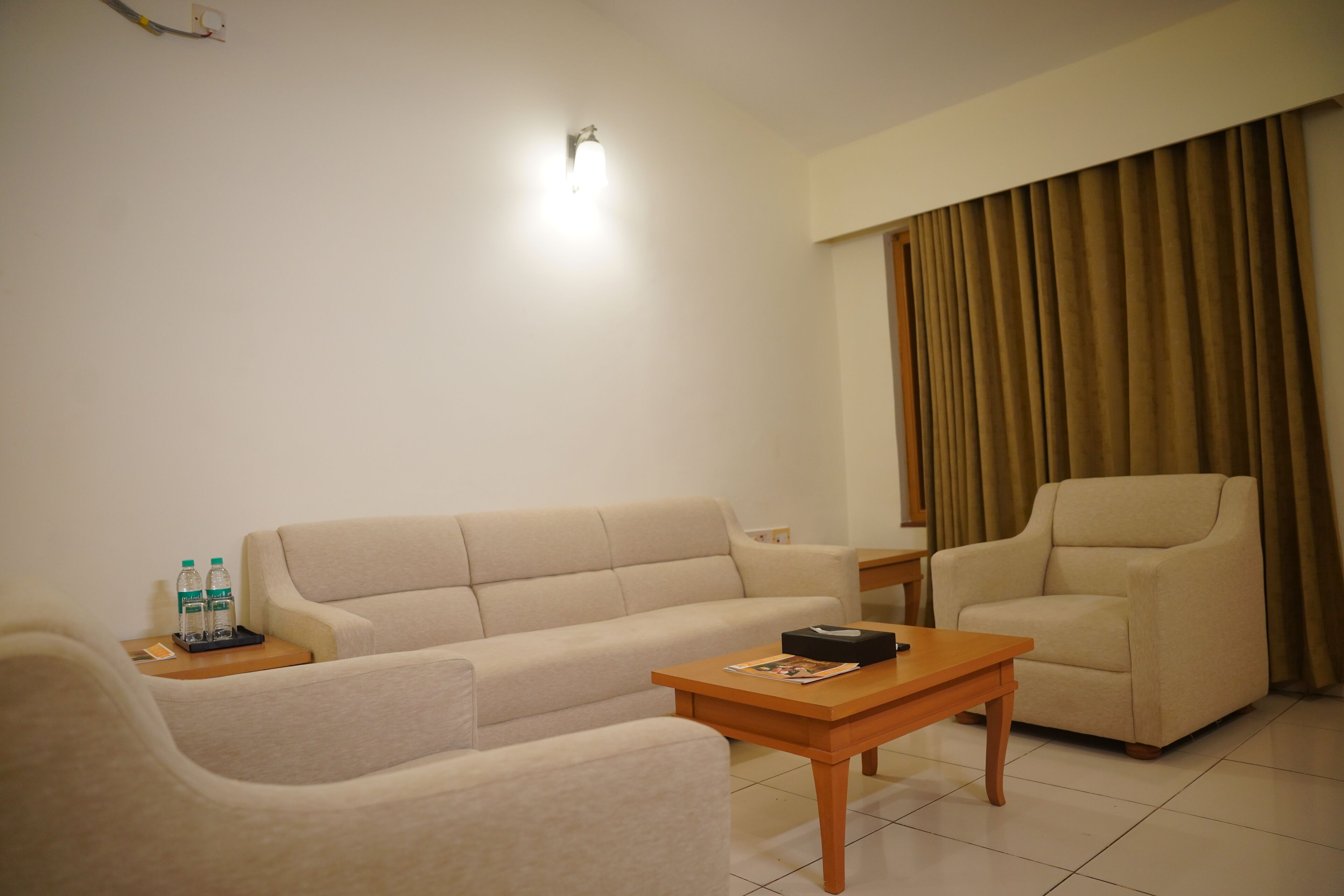 A living room with a sofa, armchair, and coffee table. There is a small table with two bottles and a remote control.