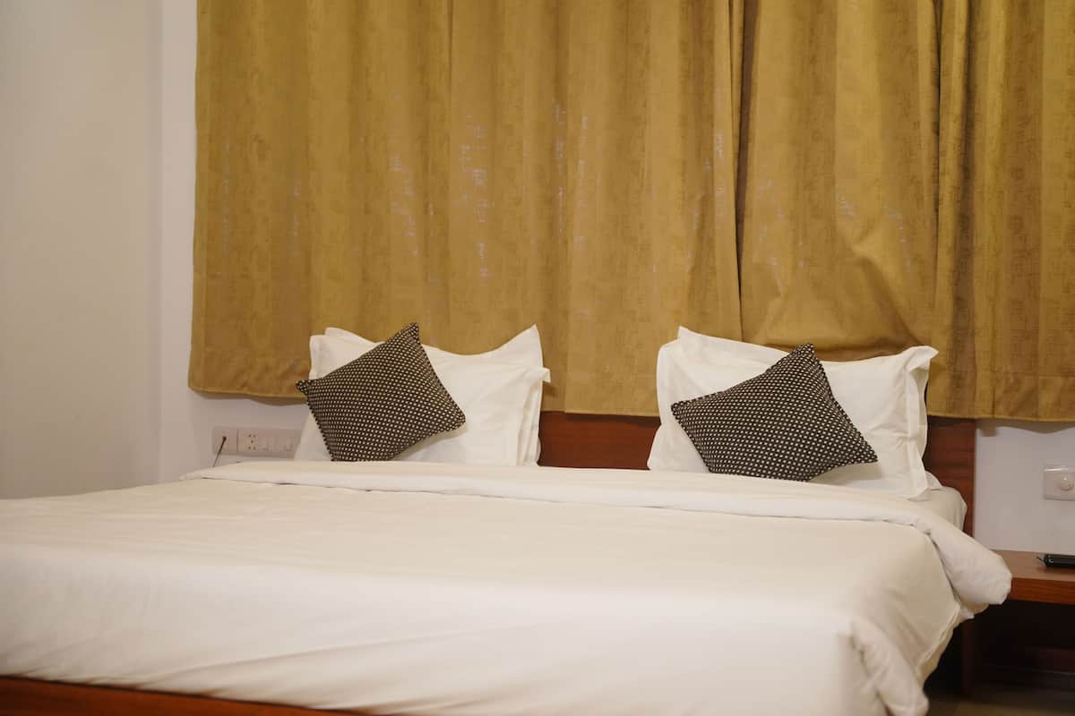 A double bed with white bedding and two patterned pillows, a wooden headboard, and a plain wall with a light switch.