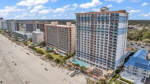 Een hoog hotel met meerdere verdiepingen, een zwembad en uitzicht op het strand.