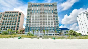 Een hoog hotel met meerdere verdiepingen, balkons en uitzicht op het strand.