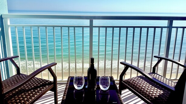 Een balkon met uitzicht op de oceaan, twee rieten stoelen, een tafel met een fles en glazen.