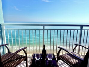 Een balkon met uitzicht op de oceaan, twee rieten stoelen, een tafel met een fles en glazen.