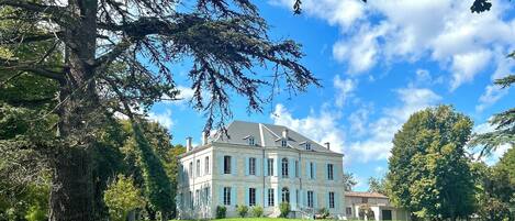 A large, historic building with a symmetrical facade, surrounded by lush green grass and trees.