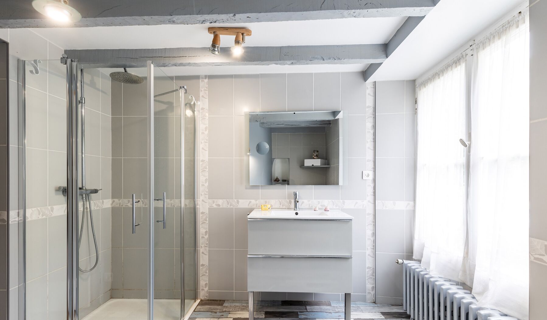 A modern bathroom with a glass-enclosed shower, a vanity with a mirror, and a radiator.