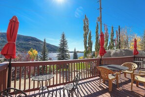 Enjoy a serene lakeside view from this outdoor deck, featuring a table and chairs under the shade of red umbrellas.