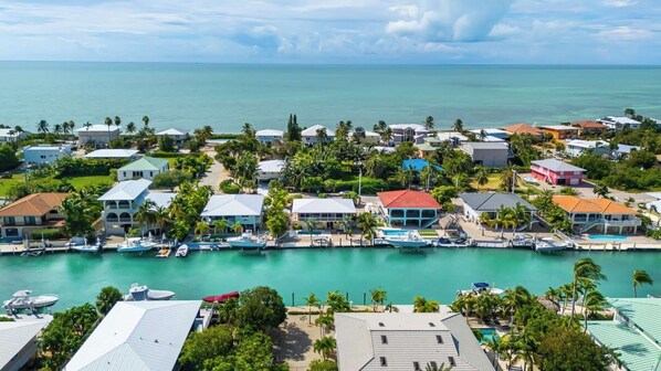 An aerial view of a coastal residential area with houses, a marina, and a clear view of the ocean.