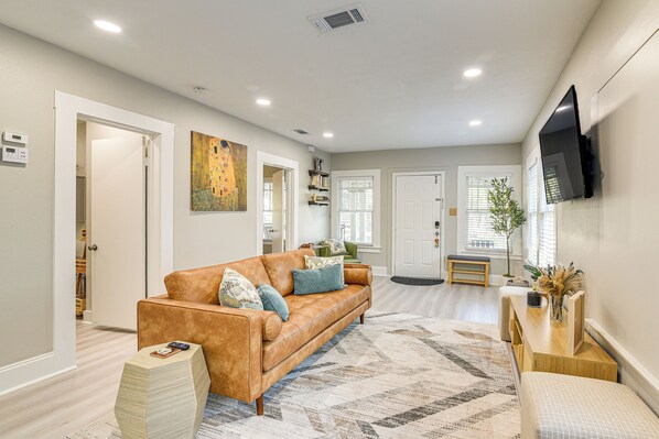 A modern living room with a leather sofa, a patterned rug, and a flat-screen TV mounted on the wall. - 3 Mi to Dtwn: Dog-friendly Home in Houston! (Houston)
