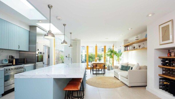 A modern kitchen with a central island, bar stools, and a dining area with a table and chairs. - Modern Living Meets Timeless Charm (Greater London)