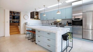 A modern kitchen with light blue cabinets, a large island with bar stools, stainless steel appliances, and pendant lighting. - Modern Living Meets Timeless Charm (Greater London)