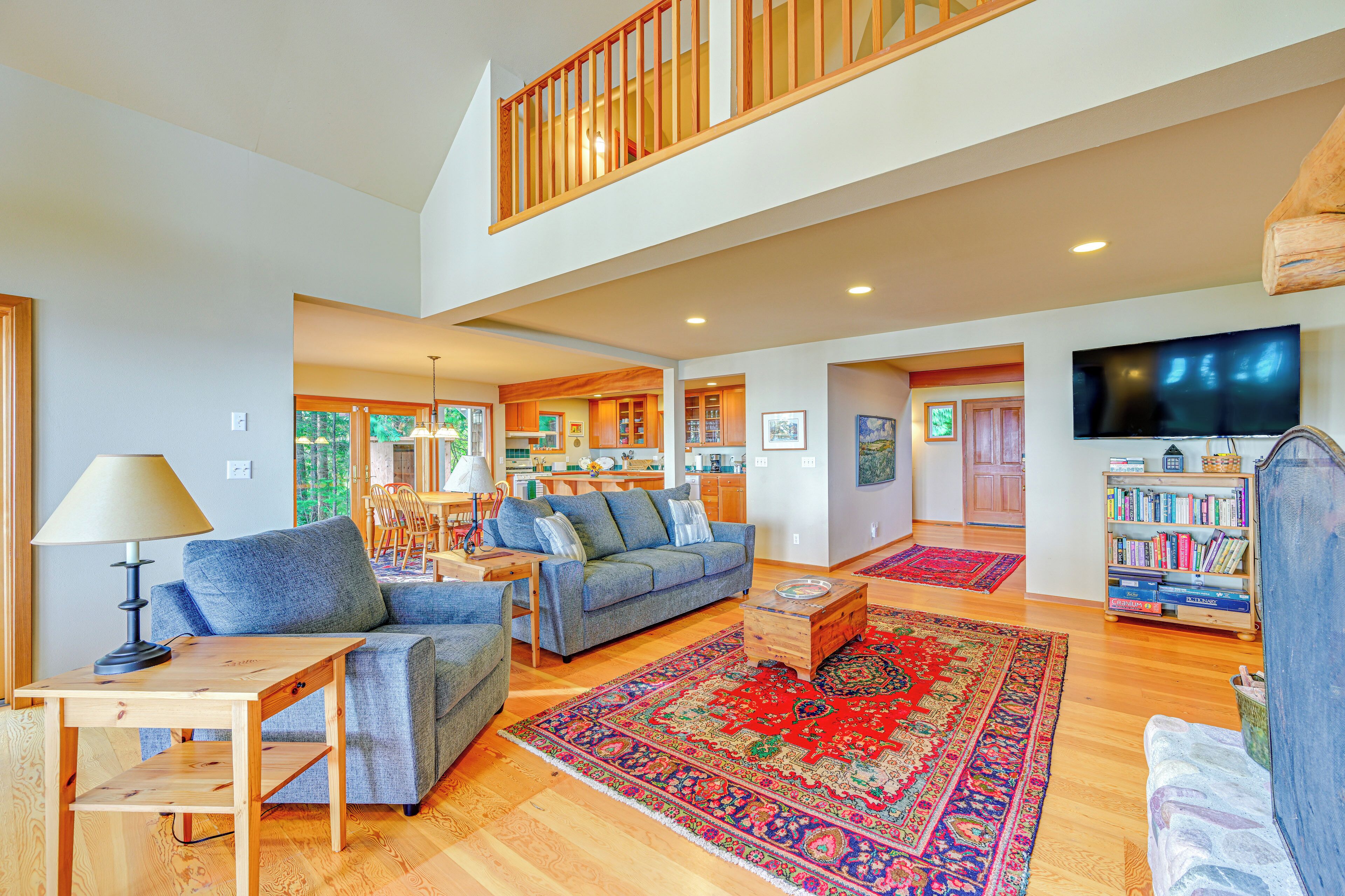A spacious living area with a high ceiling, wooden flooring, a blue sofa, a wooden coffee table, and a red patterned rug.