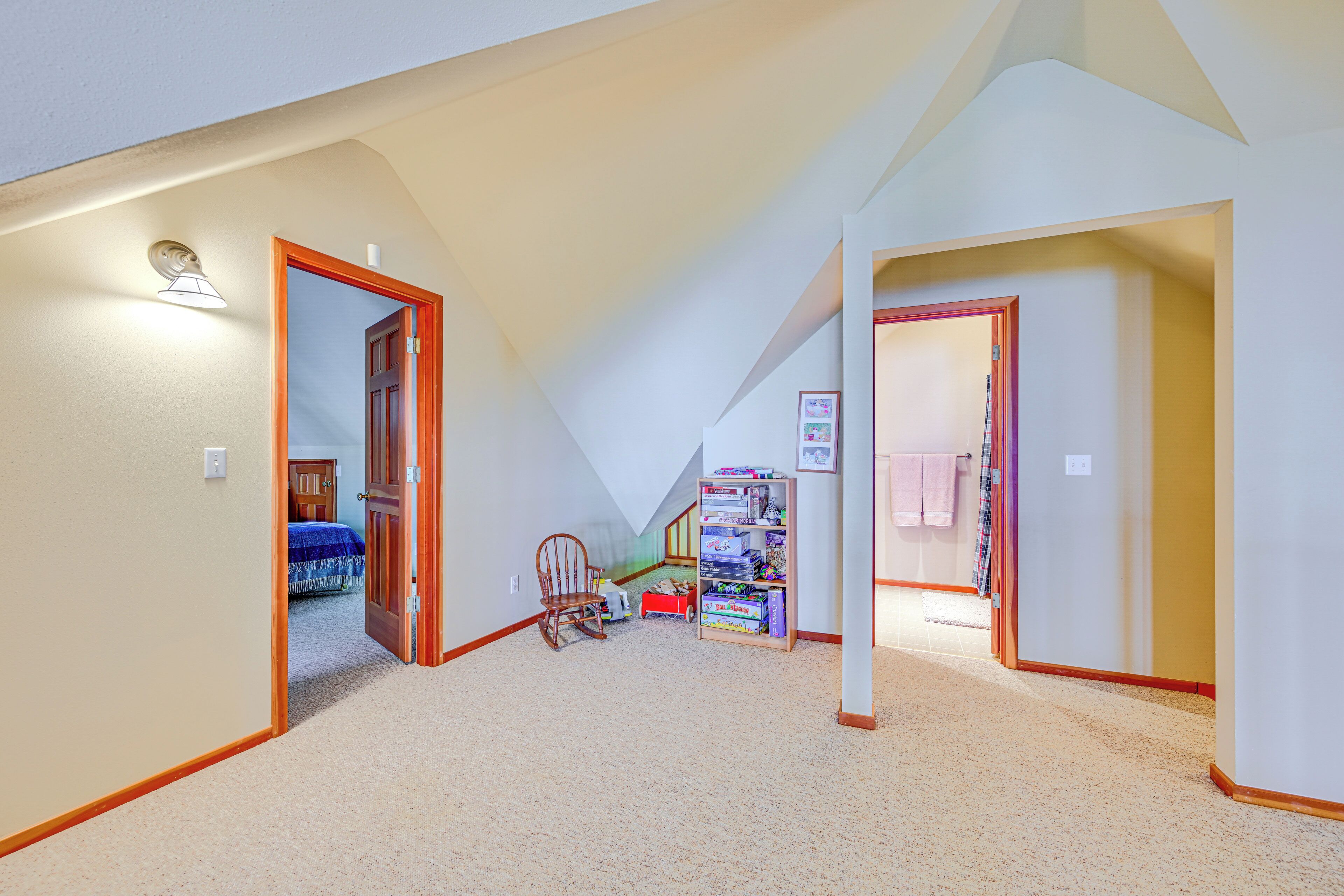 A spacious attic room with a sloped ceiling, a wooden rocking chair, and a collection of board games.