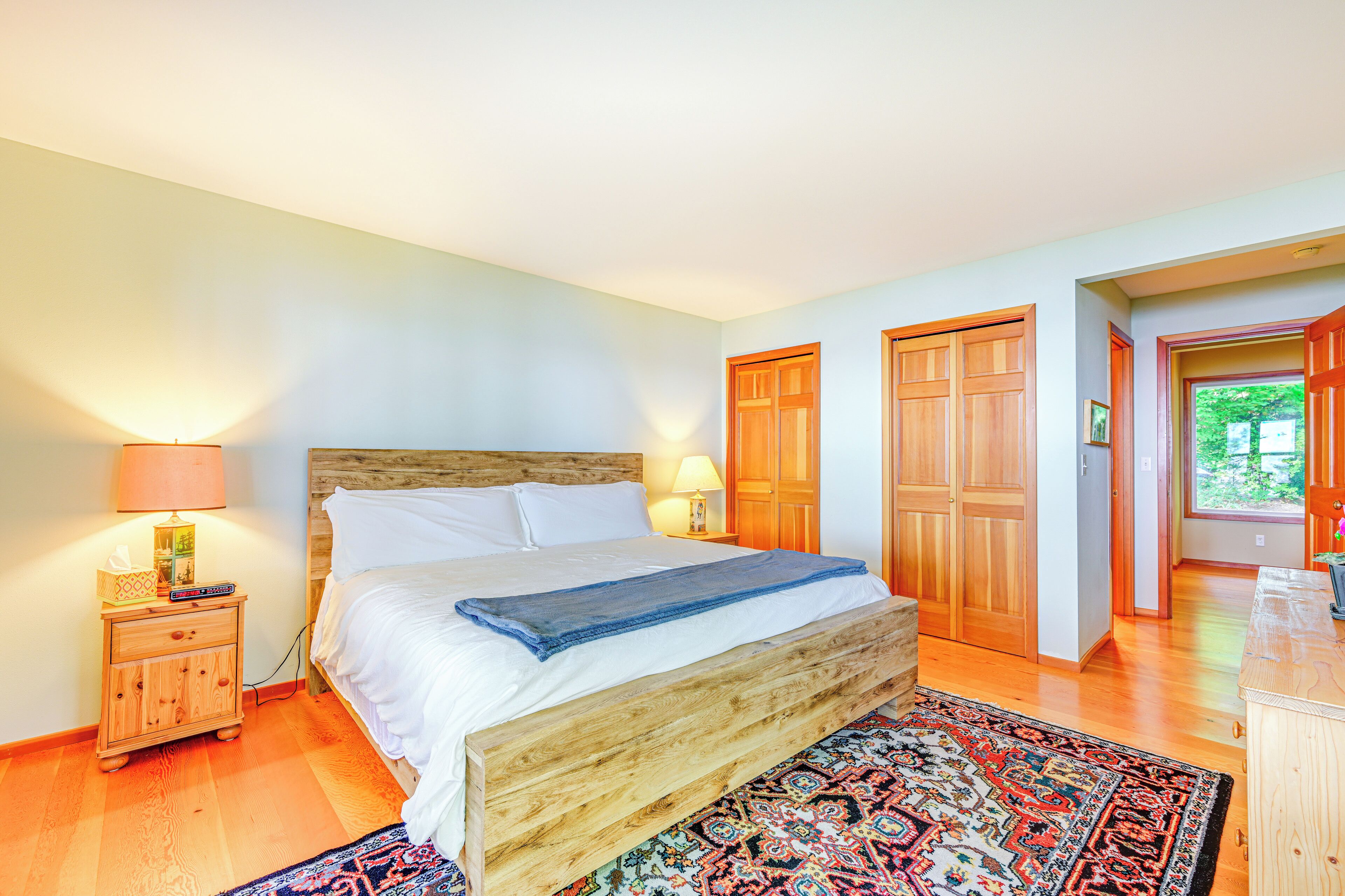 A bedroom with a wooden bed, a nightstand with a lamp, a patterned rug, and wooden doors.
