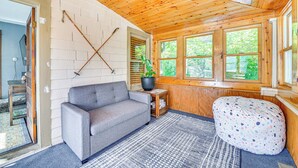 A cozy room with a gray sofa, a patterned bean bag, a small table with a potted plant, and a window with a view of greenery. - Pet-friendly Catskills Retreat: Fire Pit & Deck! (Grand Gorge)