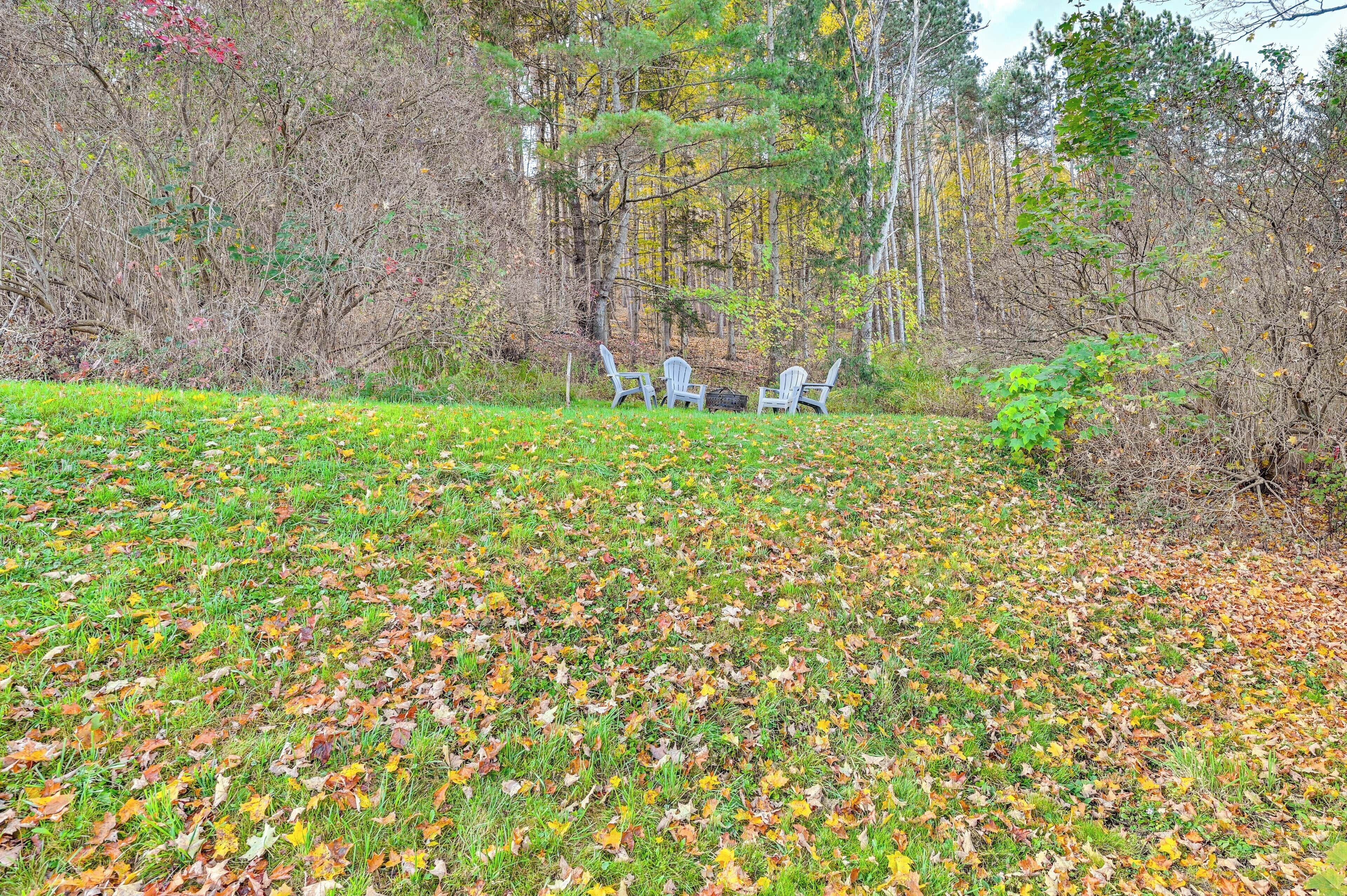 A grassy area with scattered leaves and three white chairs in the background.
