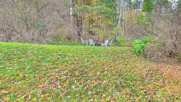 A grassy area with scattered leaves and three white chairs in the background.