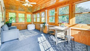 A wooden cabin interior with a ceiling fan, large windows, a sofa, a desk, and a chair. - Pet-friendly Catskills Retreat: Fire Pit & Deck! (Grand Gorge)