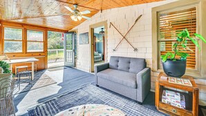 A cozy room with a wooden ceiling, a gray sofa, a dining table with chairs, and a large window with blinds. - Pet-friendly Catskills Retreat: Fire Pit & Deck! (Grand Gorge)