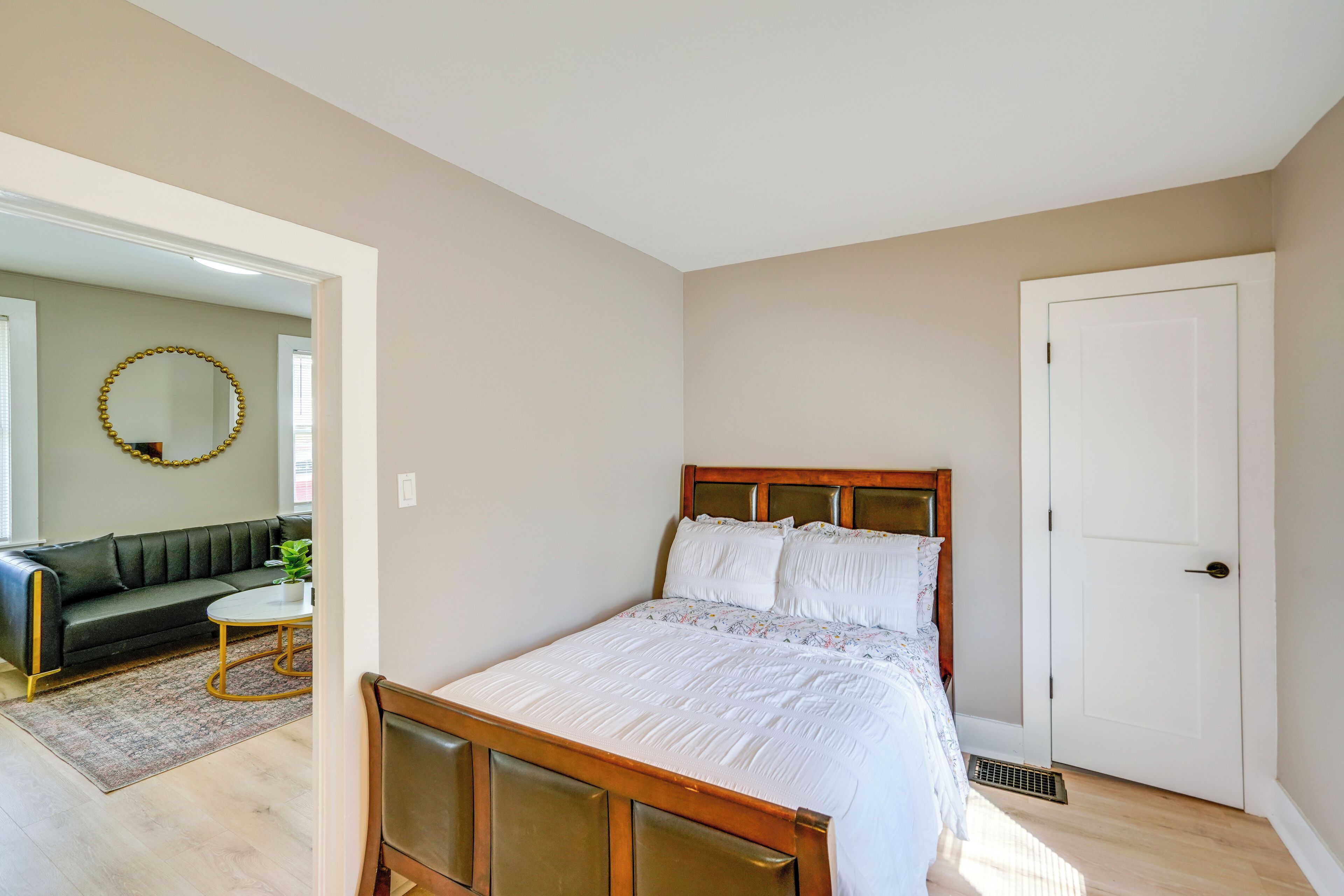A bedroom with a wooden bed, a white door, and a living area with a sofa and a coffee table.