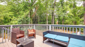 A wooden deck with wicker furniture, including a sofa and chairs, overlooking a forested area. - Family Home w/ Deck & Game Room in Stockbridge! (Stockbridge)